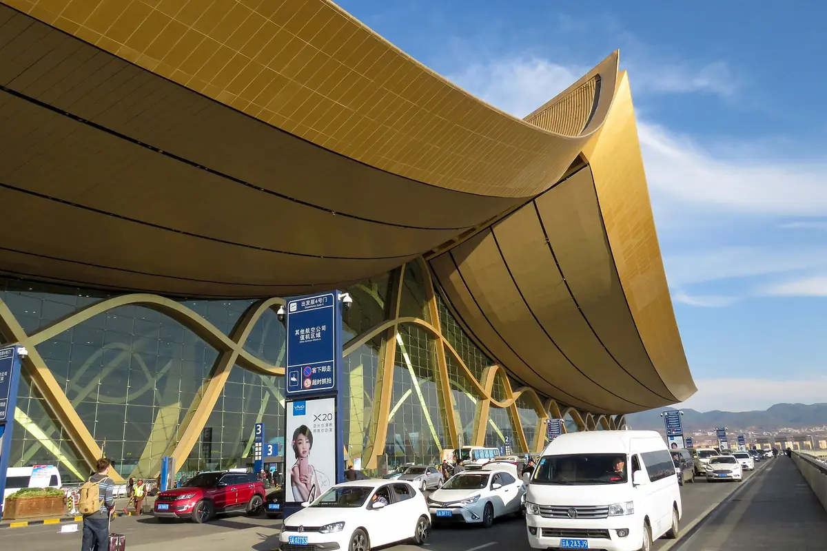 Techo dorado y curvo del aeropuerto sobre una carretera con coches y furgonetas blancas