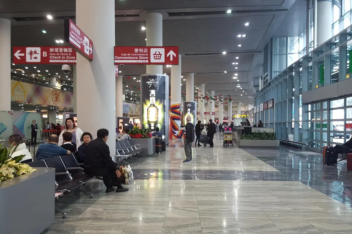 Pasajeros sentados en una sala del aeropuerto bajo señales direccionales rojas
