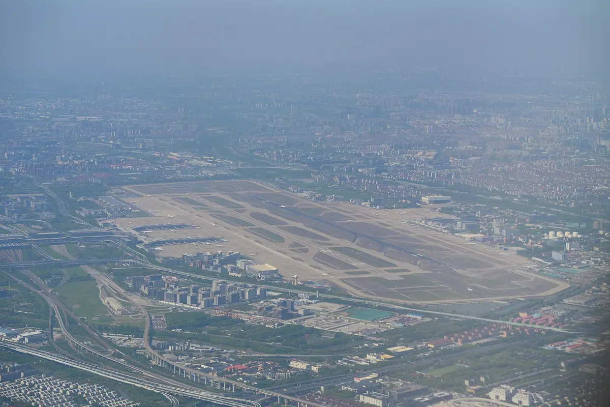 Aerial view of airport runways and terminal buildings beneath a hazy city skyline
