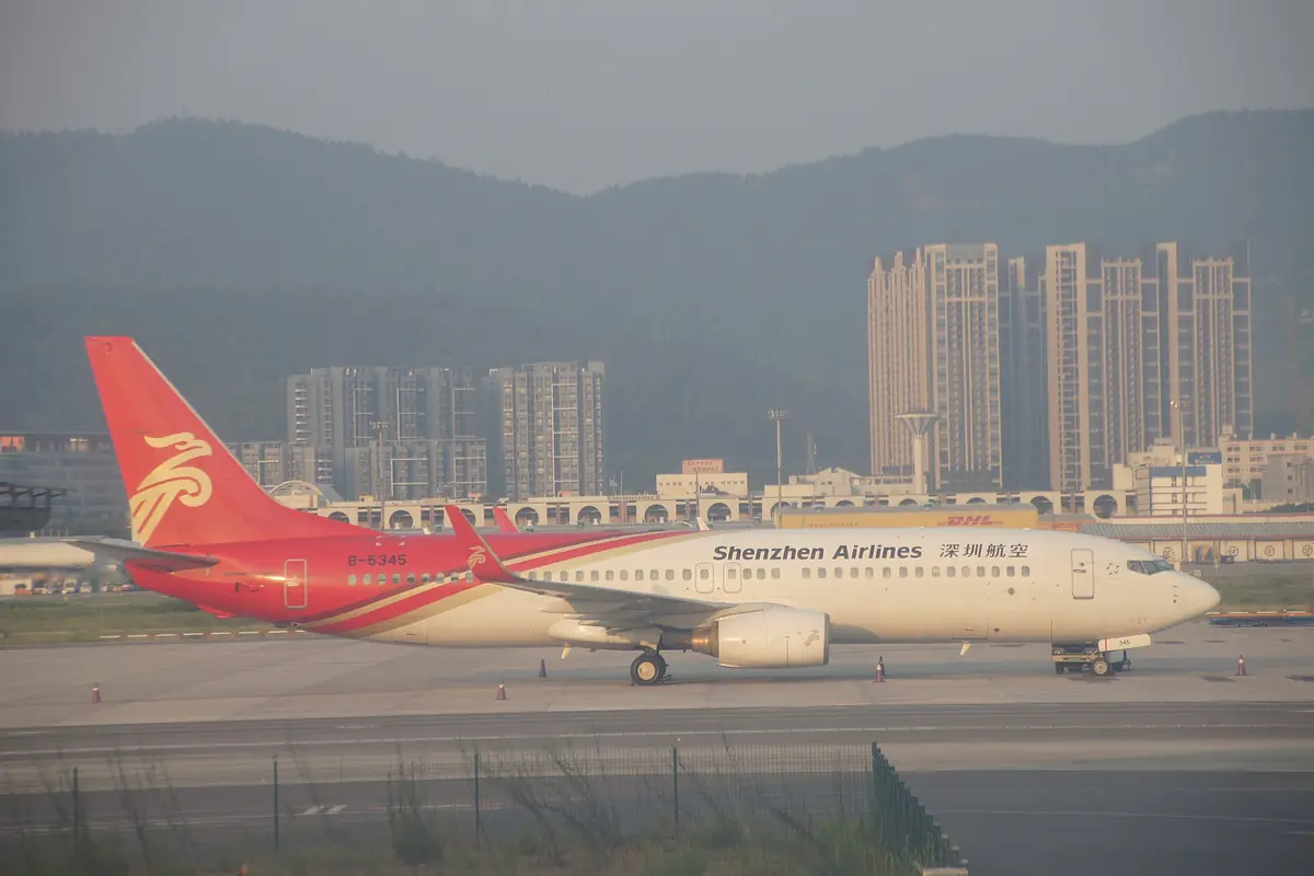 Shenzhen Airlines passenger jet taxiing with apartment towers and hills behind it