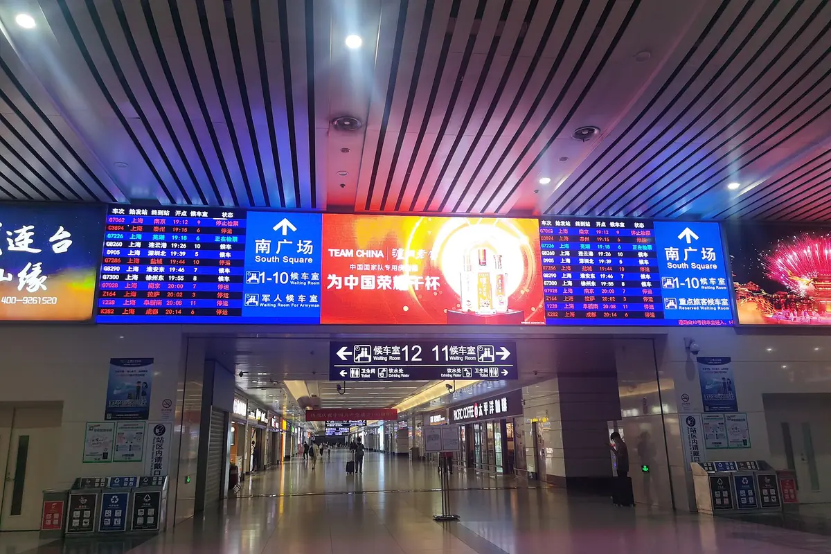 Bahnhofshalle mit blauen Informationstafeln und einem leuchtend roten Banner unter der Decke