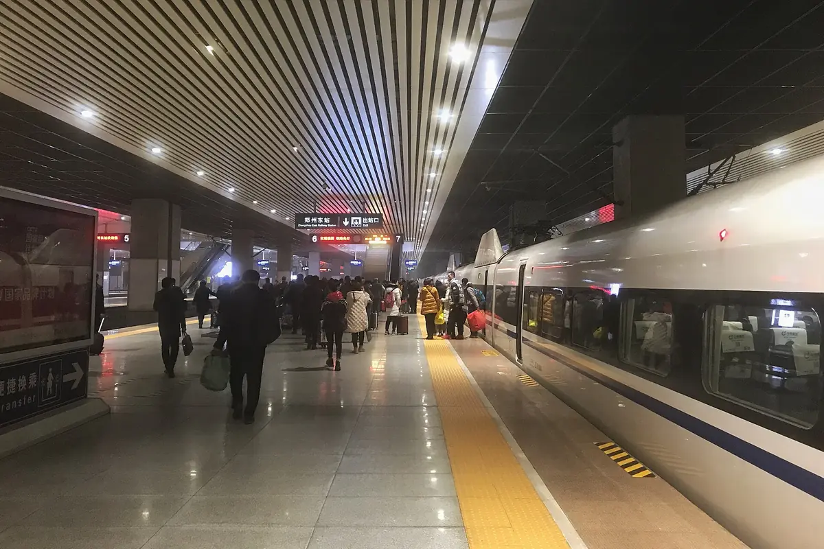 Pasajeros caminando entre trenes en un andén bajo filas de luces en el techo