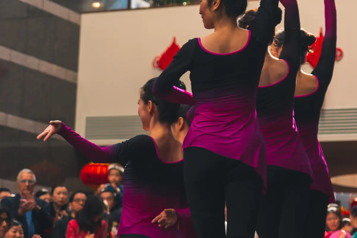 Dancers in black-and-magenta costumes performing before a seated audience