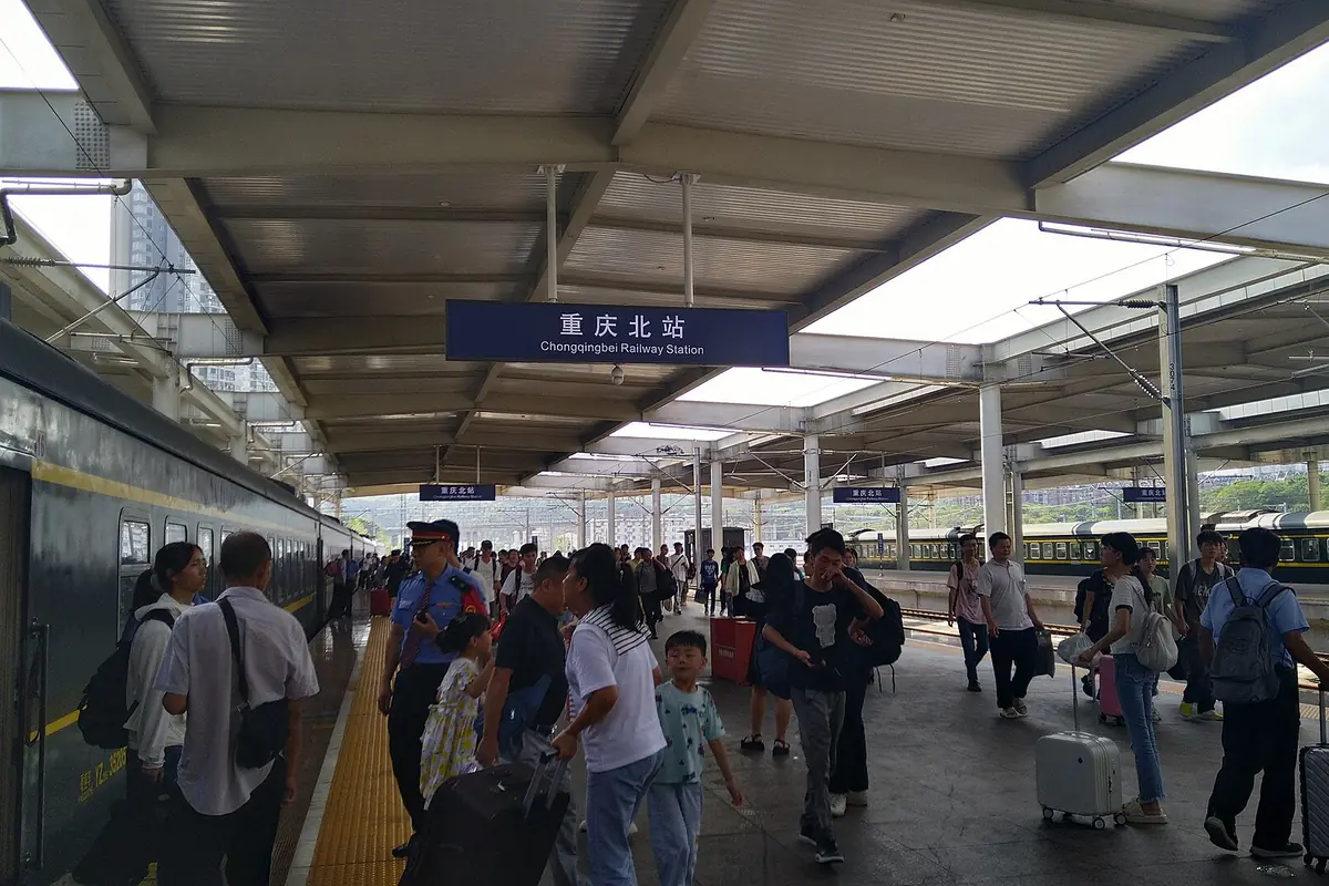 Viajeros esperan con equipaje bajo la cubierta de una estación de tren