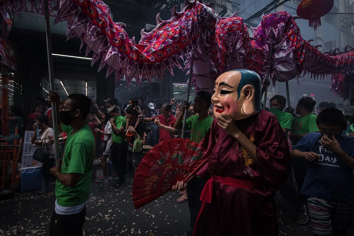 Masked festival performer beneath a long red dragon carried through a crowd