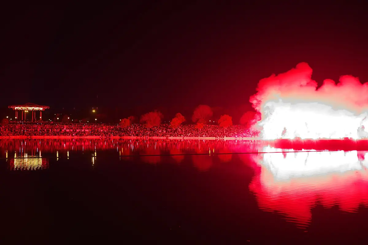 Red fireworks and bright smoke reflected across a lake at night