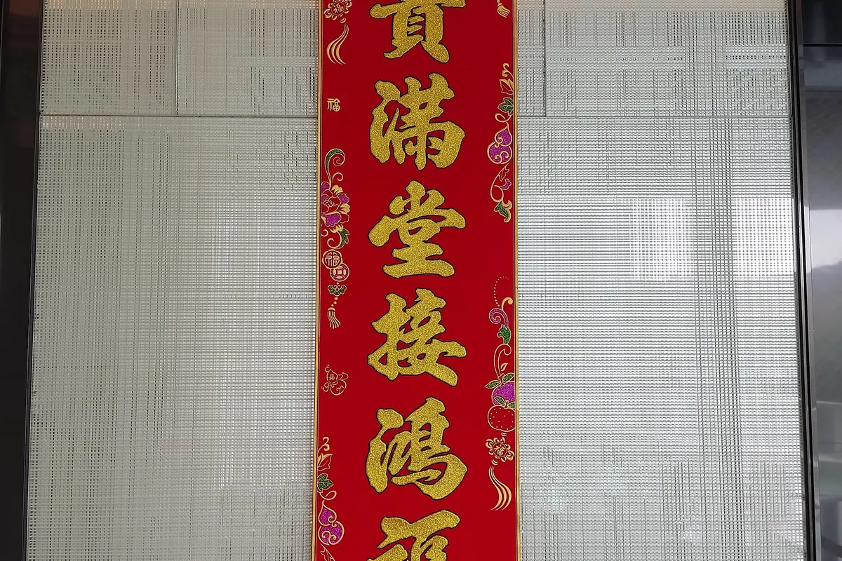 Vertikales rotes Banner mit goldener chinesischer Kalligrafie an einem Fenster
