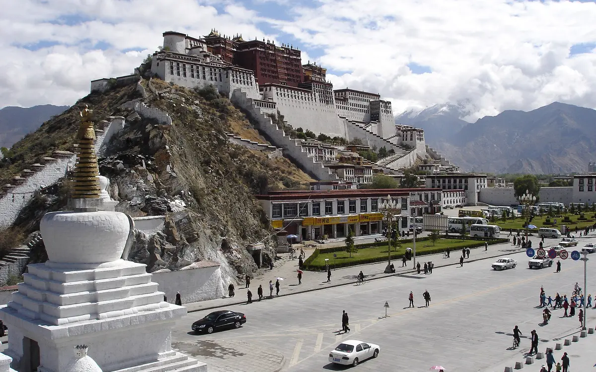 Potala Palace above a broad road and white stupa beneath cloudy skies in Lhasa