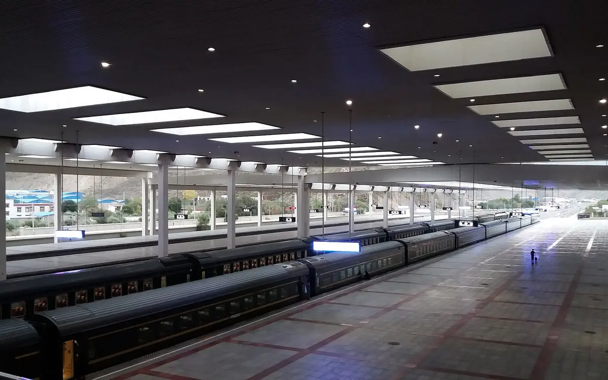 Long passenger train beside an empty platform beneath a brightly lit station roof