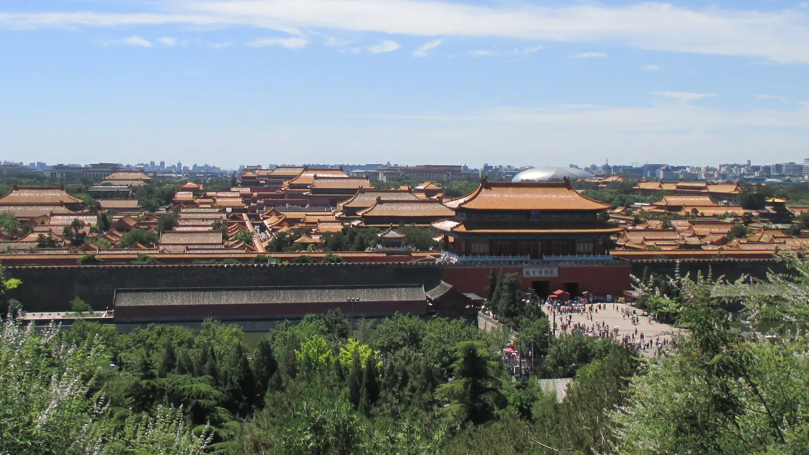 Golden roofs and red palace halls of the Forbidden City beyond green trees in Beijing