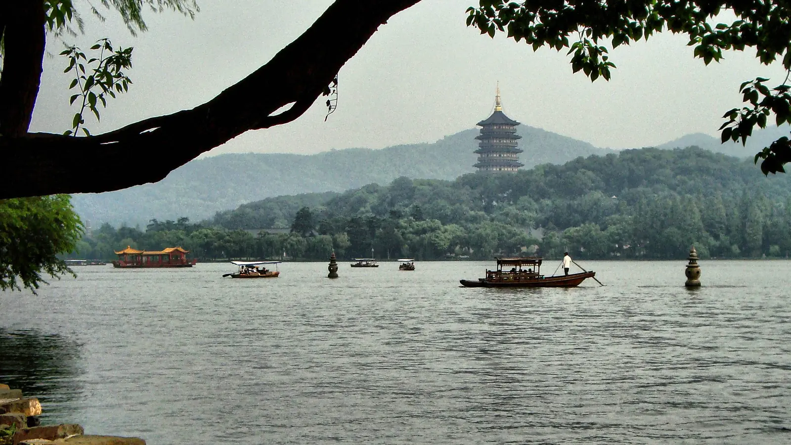 Small boats on West Lake beneath a distant pagoda and overhanging branches in Hangzhou