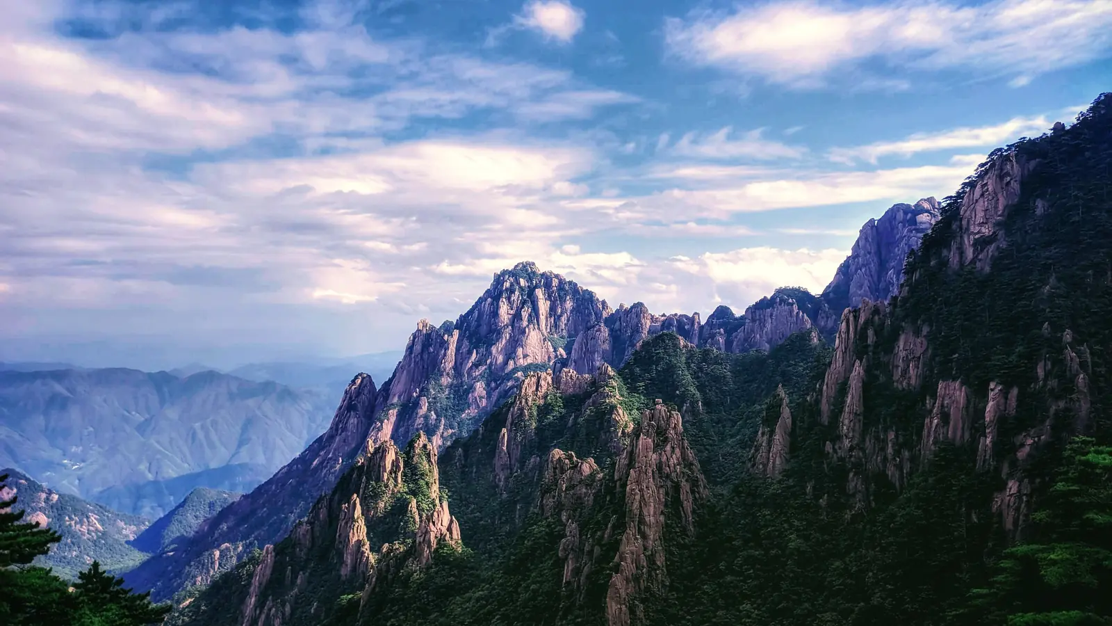 Jagged granite peaks and pine-covered slopes beneath pastel clouds on Huangshan, Anhui
