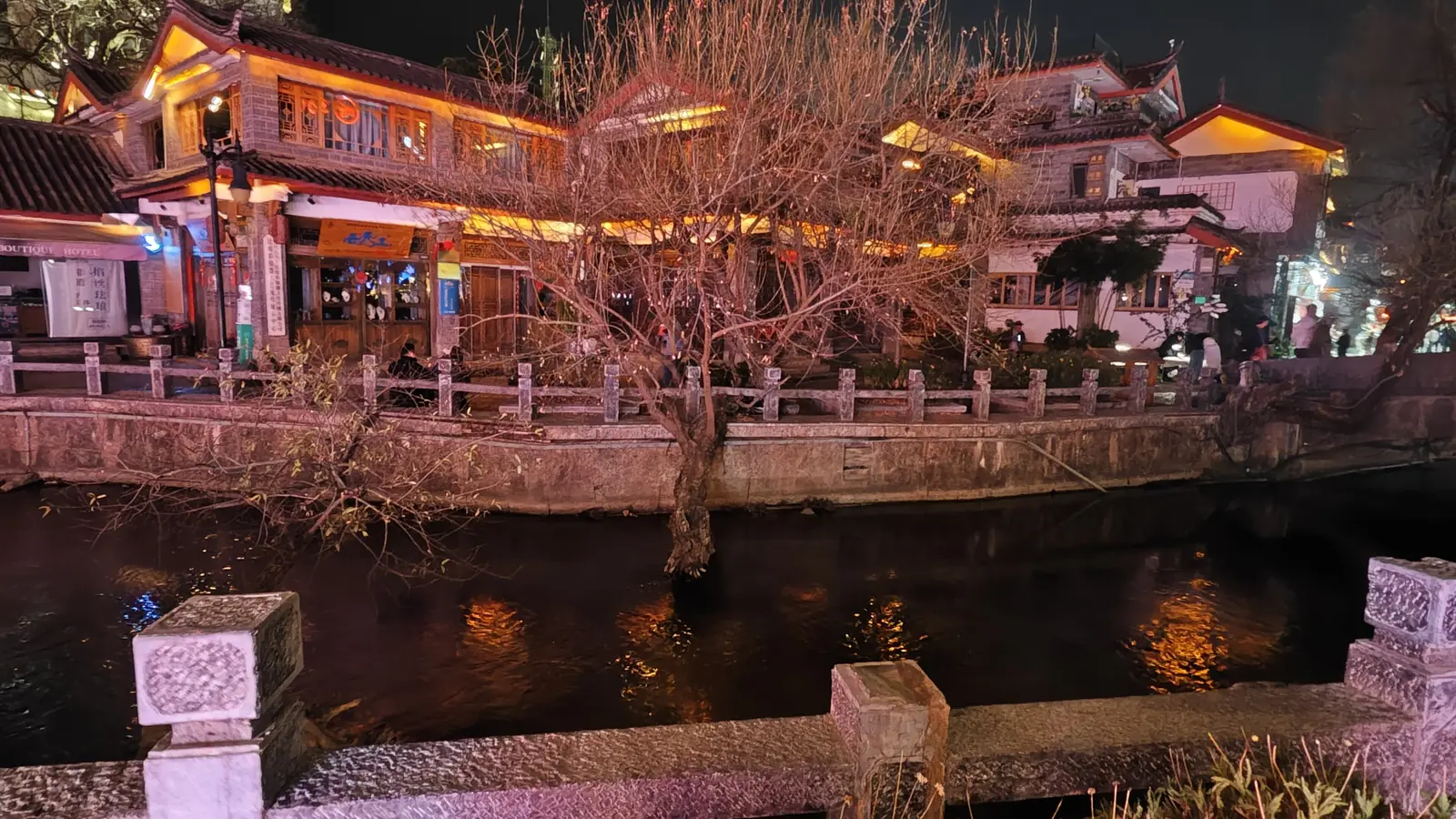 Lantern-lit wooden buildings beside a stone bridge and canal in Lijiang Old Town, Yunnan