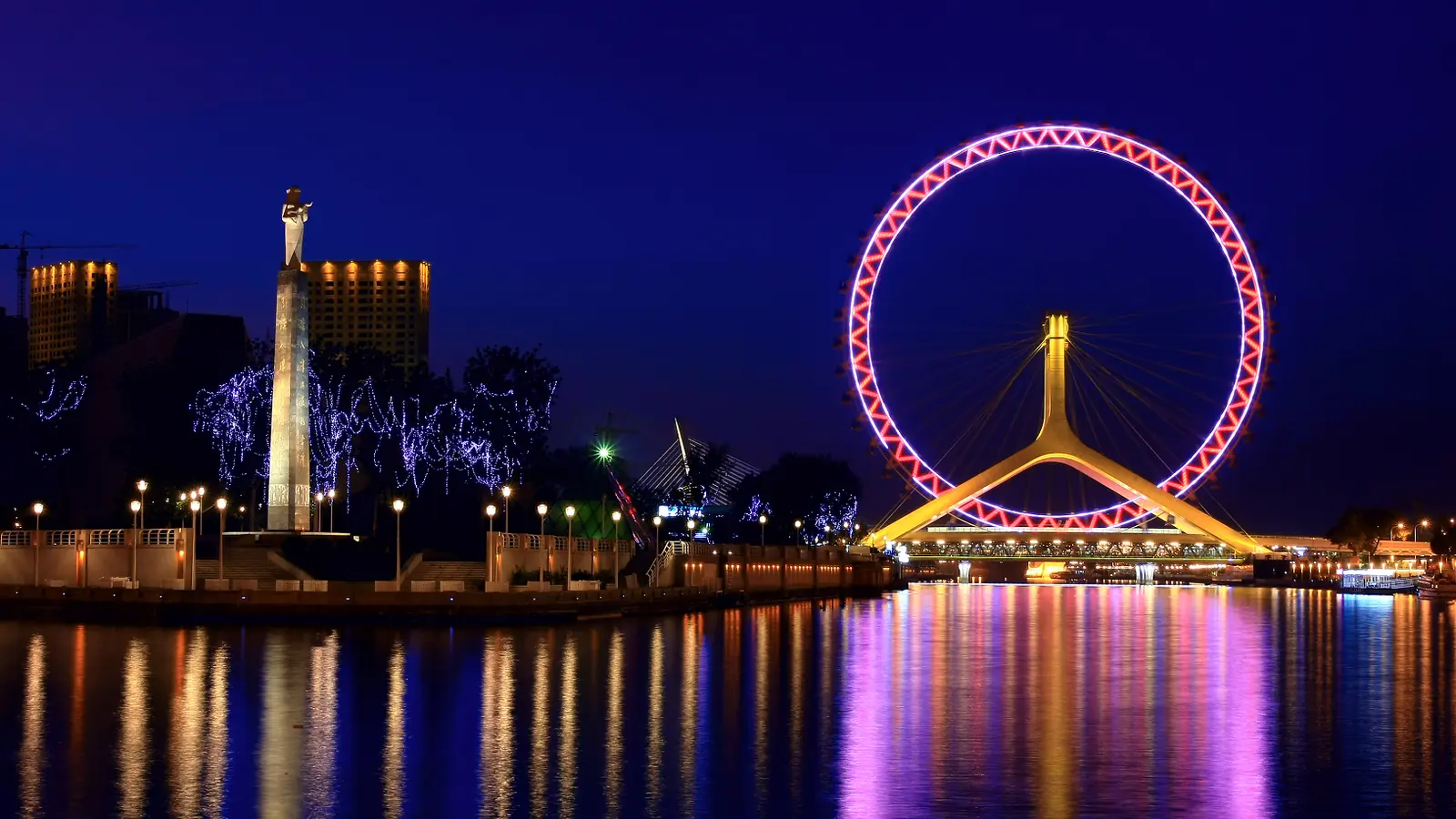 Tianjin Eye Ferris wheel illuminated in pink above reflections on the Hai River at night