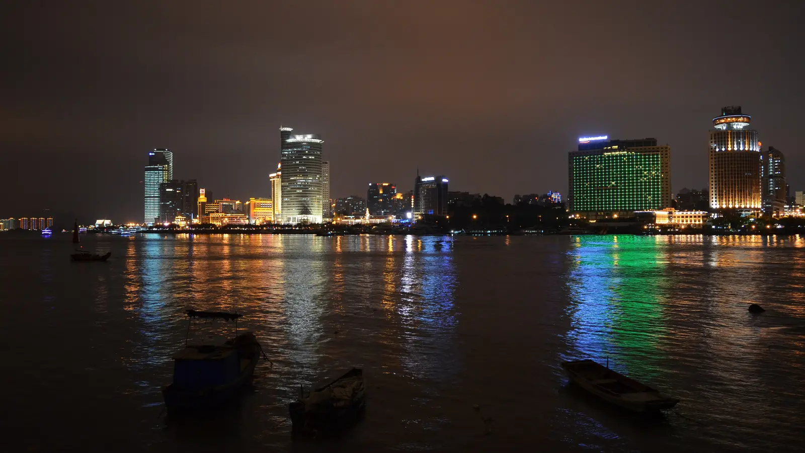 Xiamen waterfront buildings reflected in dark harbor water at night