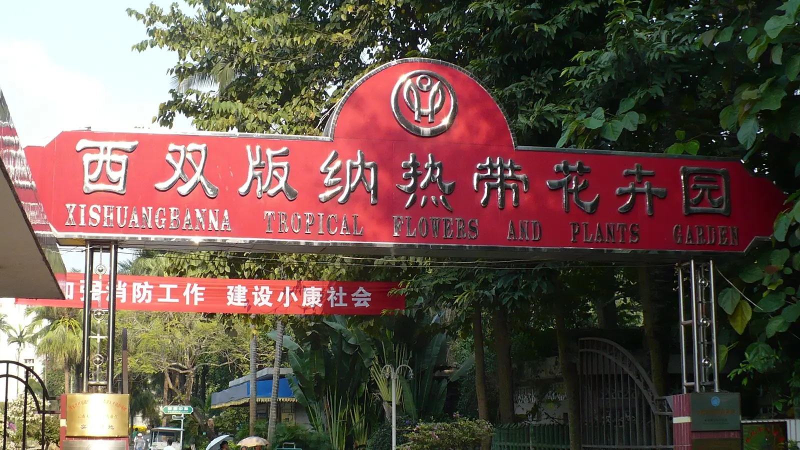 Red Xishuangbanna Tropical Flower Garden entrance sign among green trees
