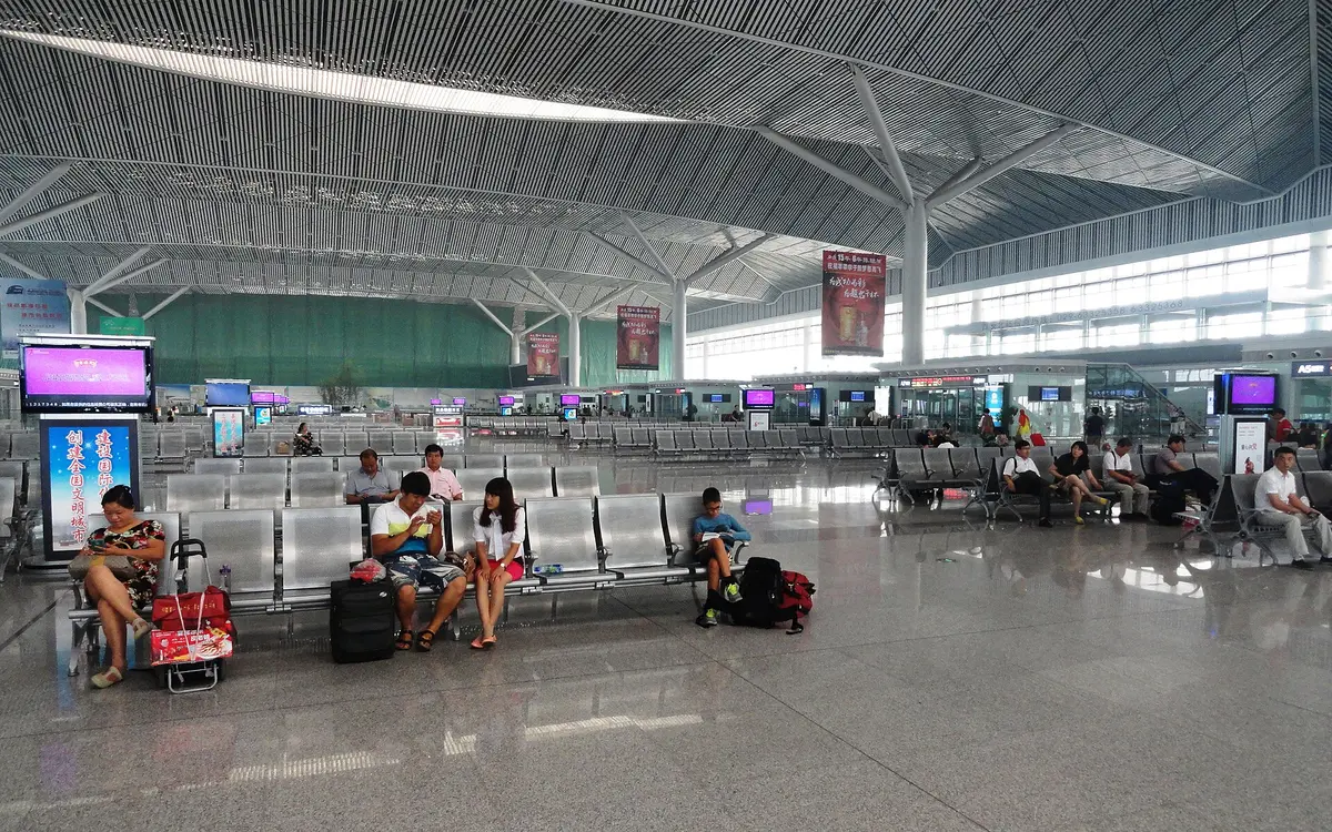 Travelers and luggage in a bright railway hall beneath an arched glass ceiling