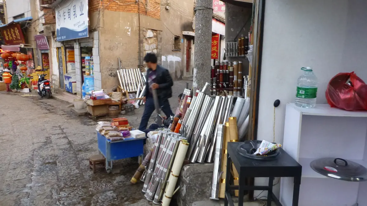 Small shop displaying long decorative pipes beside pedestrians on a narrow lane