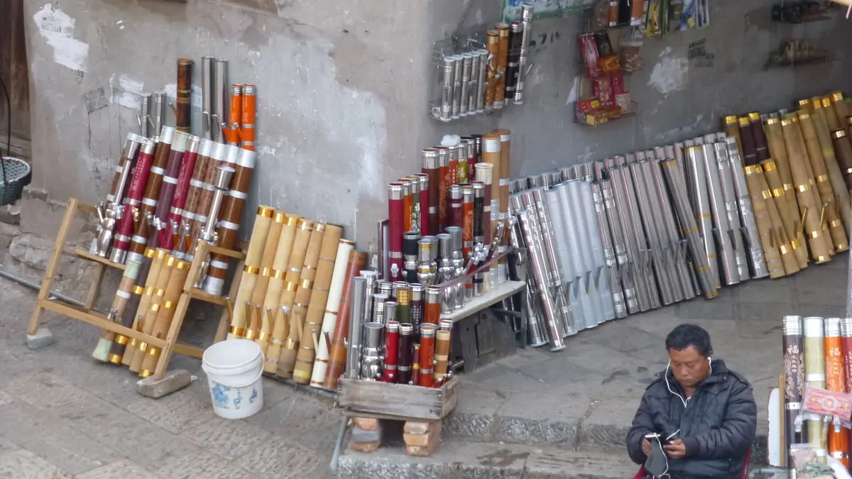 Vendedor sentado junto a largas pipas decorativas e instrumentos musicales delante de una tienda