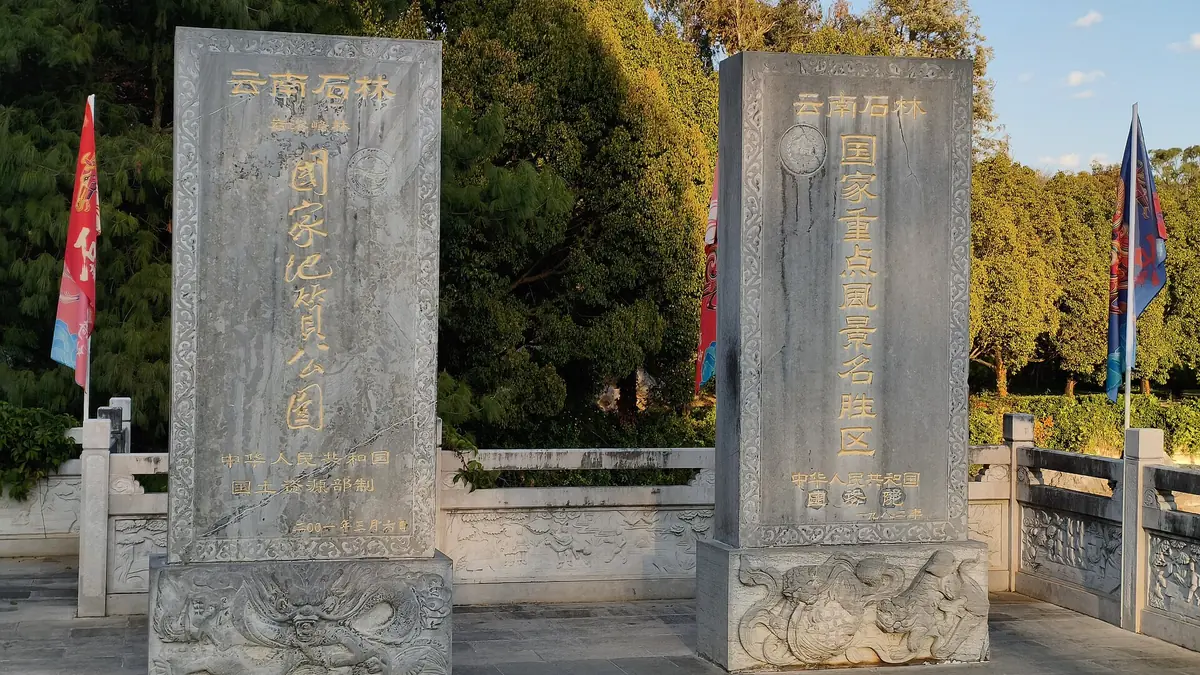 Two tall stone steles with gold inscriptions beside autumn-colored trees