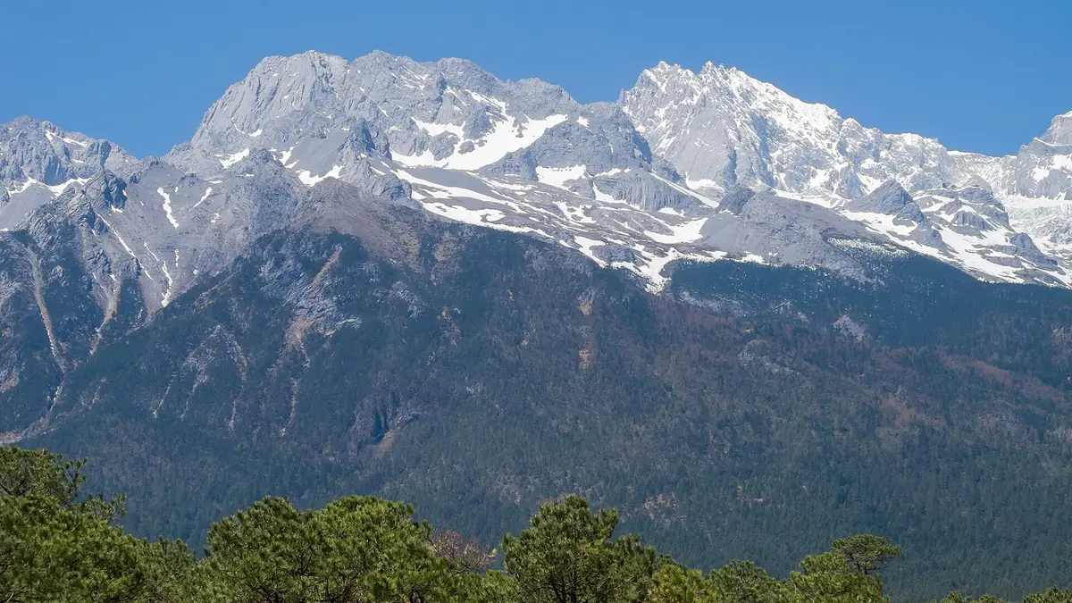 Snow-covered mountain peaks rising above dark wooded foothills