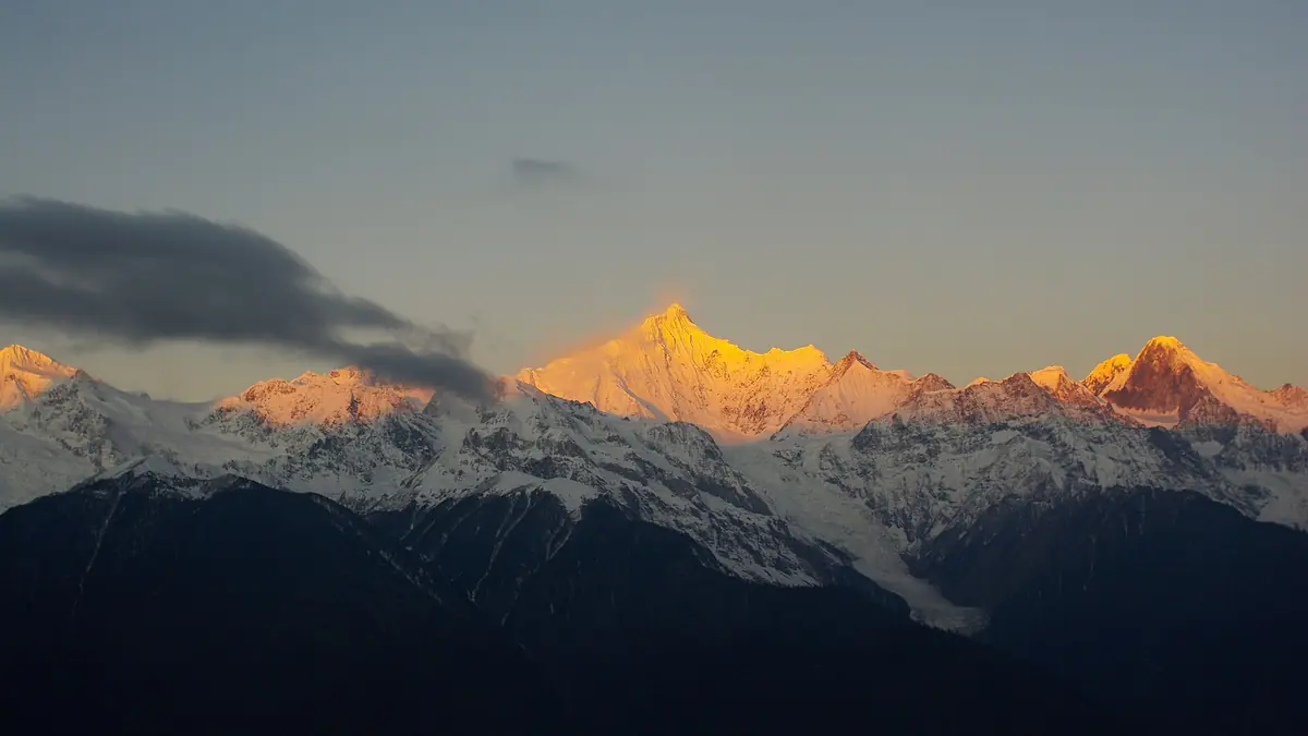 Cahaya matahari terbit mewarnai puncak gunung bersalji keemasan di atas kaki bukit yang gelap