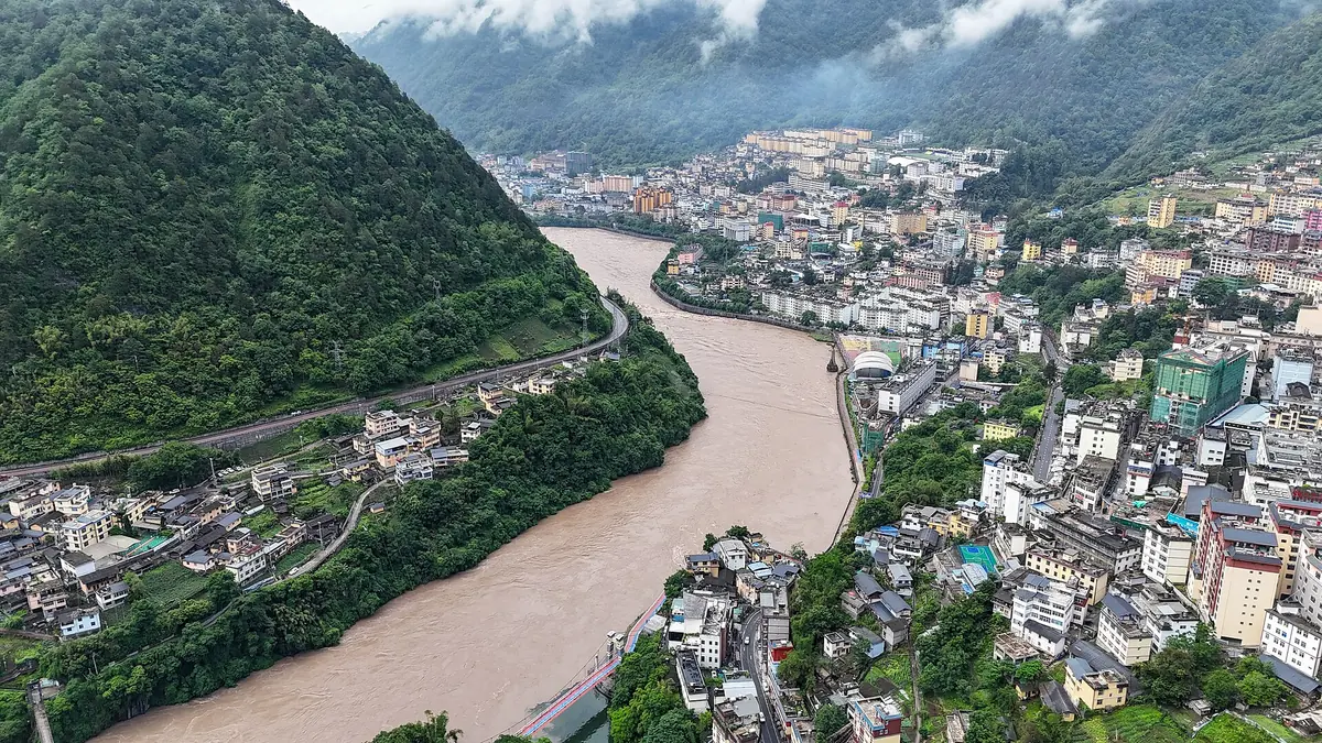 Aerial view of a muddy river curving through a town between steep green mountains