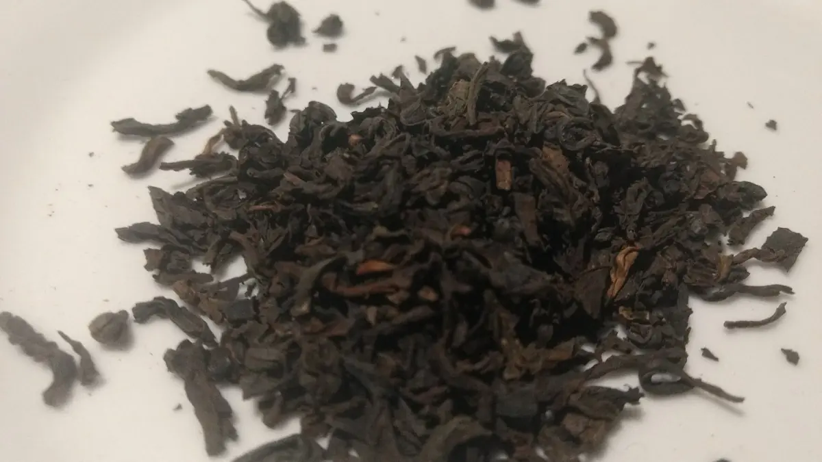 Timbunan daun teh gelap yang belum digulung di permukaan pucat