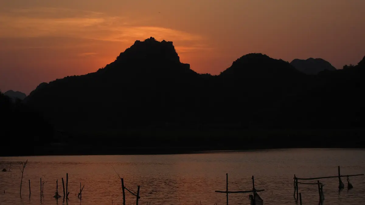 Colinas kársticas recortadas sobre un lago bajo un cielo anaranjado al atardecer