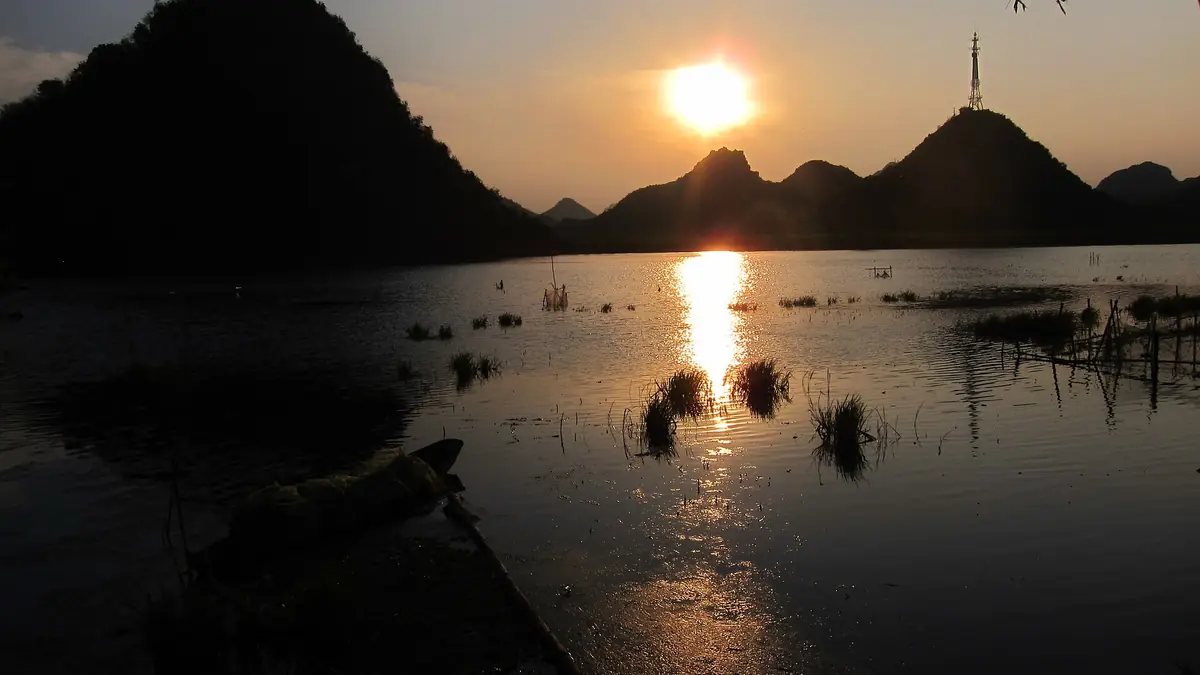 El sol se refleja en un lago entre oscuras colinas kársticas al anochecer