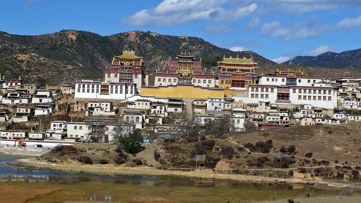 Bangunan Tibet berwarna putih dan merah dengan bumbung keemasan di bawah lereng gunung yang kering