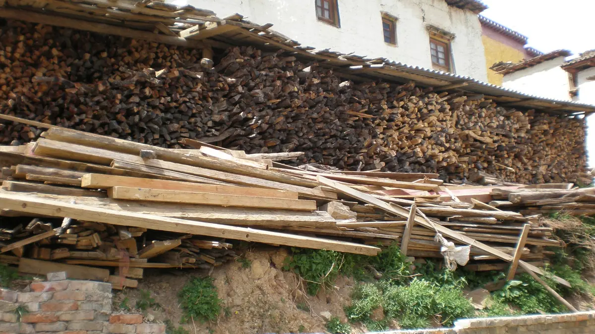 Kayu api bertindan dan tiang kayu panjang di luar rumah kampung berwarna putih