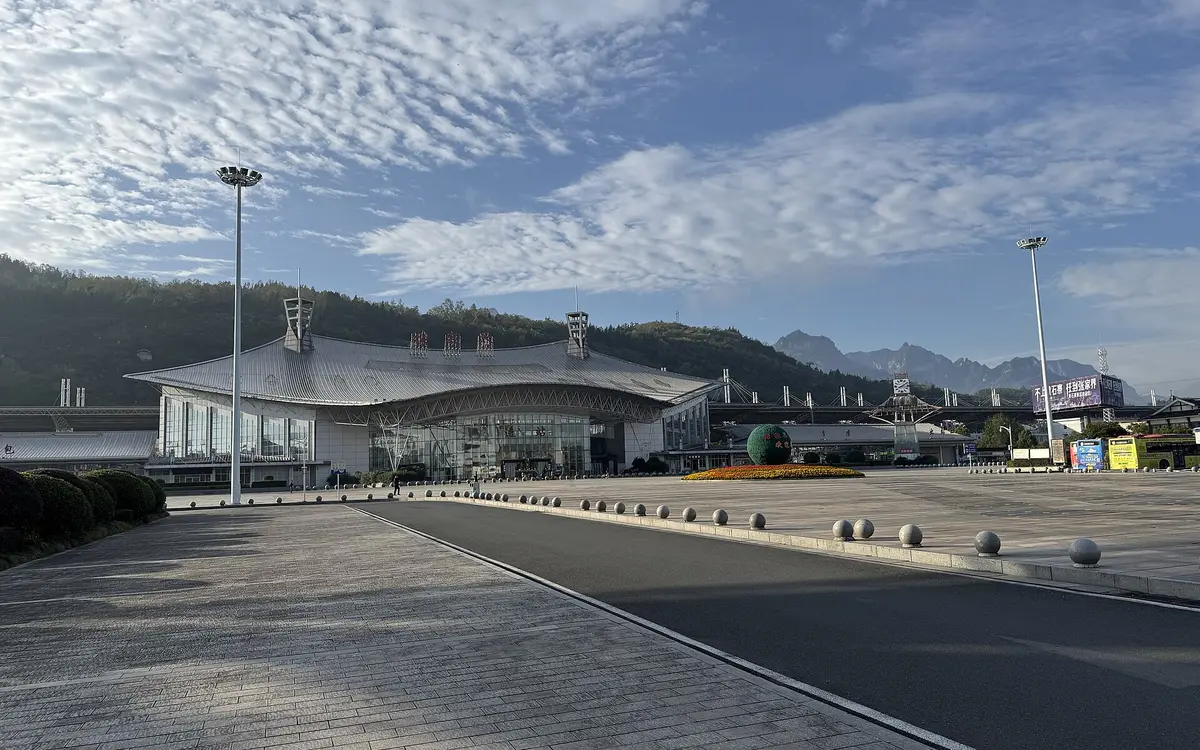 Low railway station and broad roadway beneath patterned clouds and distant hills