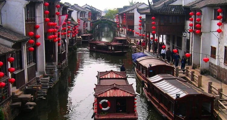 Covered wooden boats in a Zhouzhuang canal beneath red lanterns and a stone bridge