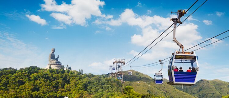Cable car cabins above wooded hills with the Tian Tan Buddha in the distance on Lantau Island