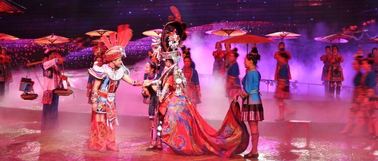 Penghibur berbaju tradisional berwarna-warni menari di bawah lampu pentas merah jambu di Sanjiang, Guangxi