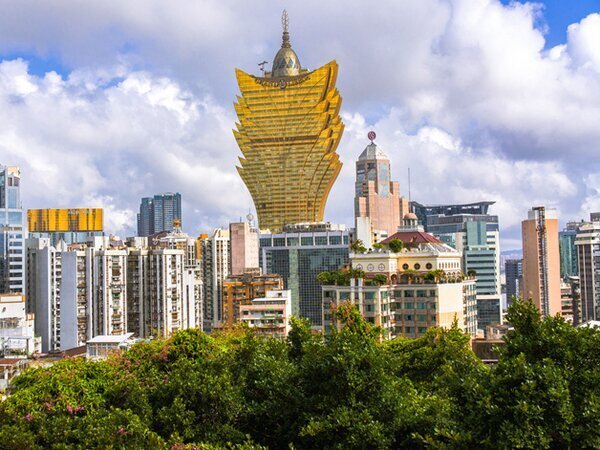 Golden fan-shaped Grand Lisboa tower rising above green trees and city buildings in Macau
