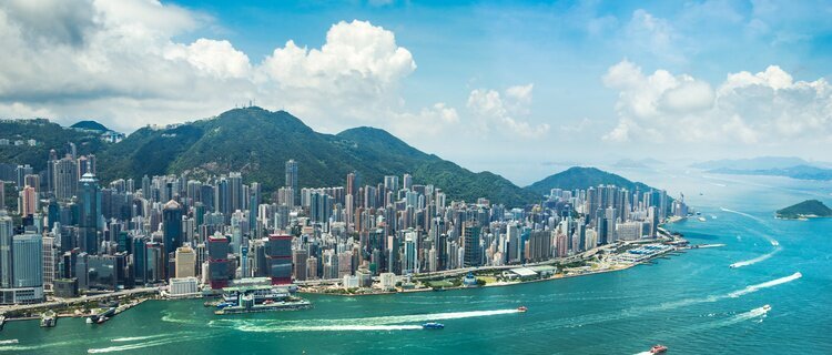High-rise buildings along Victoria Harbour with green hills and ferry wakes in Hong Kong